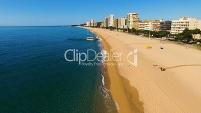 Aerial view of the boat at the yellow sandy beach with people on the coast on a hot sunny day. Spain, Catalonia