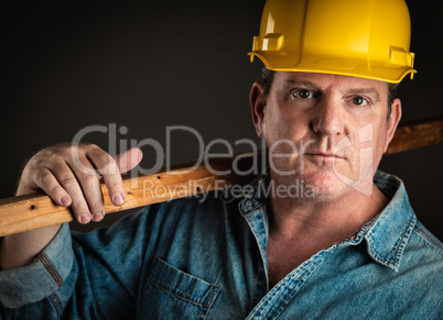 Serious Contractor in Hard Hat Holding Plank of Wood With Dramat