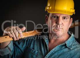 Serious Contractor in Hard Hat Holding Plank of Wood With Dramat