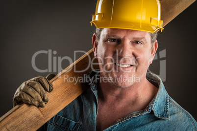 Smiling Contractor in Hard Hat Holding Plank of Wood With Dramat