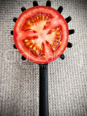Half tomato on a black plastic kitchen spoon.
