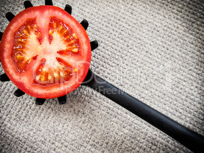 Half tomato on a black plastic kitchen spoon.