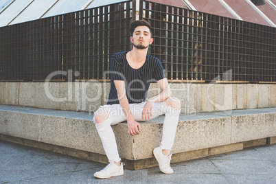 Stylish young man with a haircut in fashion  sitting in the stre