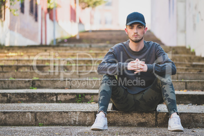 fashionable young man sitting on stairs in street