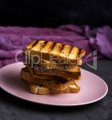 stack of square toasted bread slices lie in a pink ceramic plate