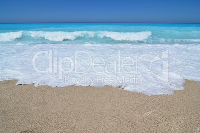 Sand, sea foam, turquoise waves and blue sky