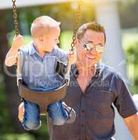 Happy Young Boy Having Fun On The Swings With His Father At The