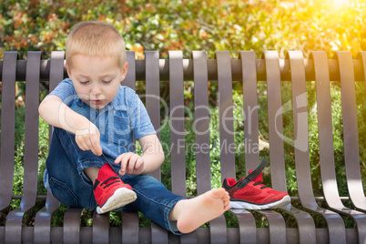 Young Boy Sitting On A Bench Putting On His Shoes At The Park