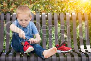 Young Boy Sitting On A Bench Putting On His Shoes At The Park