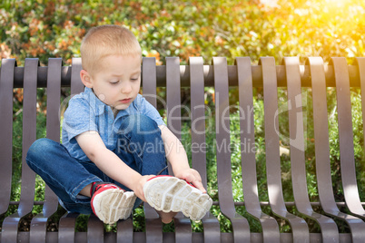 Young Boy Sitting On A Bench Putting On His Shoes At The Park