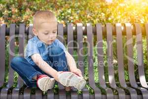 Young Boy Sitting On A Bench Putting On His Shoes At The Park