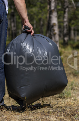 man's hand holds against a forest full of garbage a large black