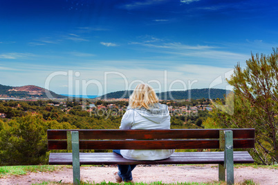 Woman on a bench, looking at a mediterranean landscape.