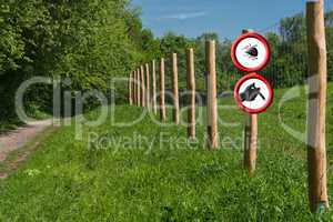 Two round red warning signs on a fence post in front of a green