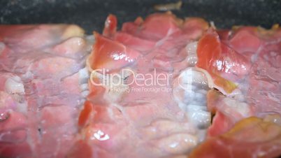 Smoked bacon being fried in a pan