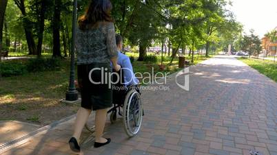 Young man on wheelchair walking with his wife outdoors