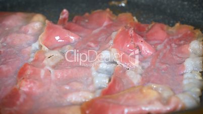 Closeup of bacon strips frying on a grill