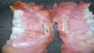 Slow motion of slices of bacon lays on the hot grill