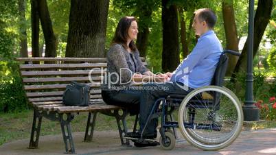 Young man on wheelchair talking with his wife in park