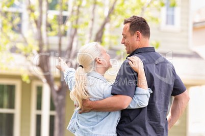 Happy Caucasian Couple Facing and Pointing to Front of House