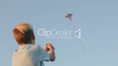 A boy launch a kite in a strong wind. In the background a kite flies in the sky. Sunset.