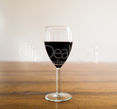 Glass of red wine on wood table against white wall.