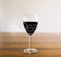 Glass of red wine on wood table against white wall.