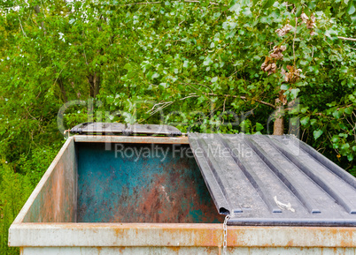 Large empty dirty metal dumpster with half-open lid.