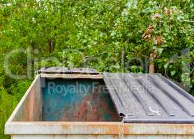 Large empty dirty metal dumpster with half-open lid.