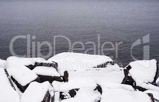 Boulders covered in snow by water.