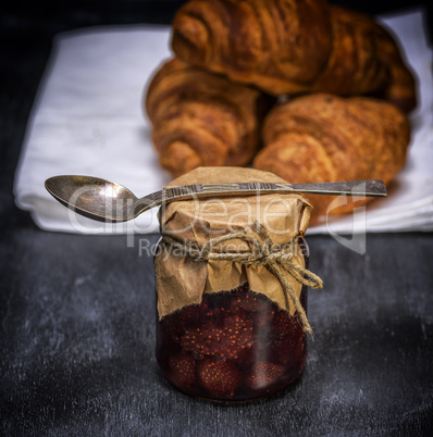 glass jar with strawberry jam and an iron spoon