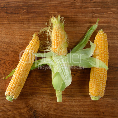 Three fresh corn cob on wooden table.