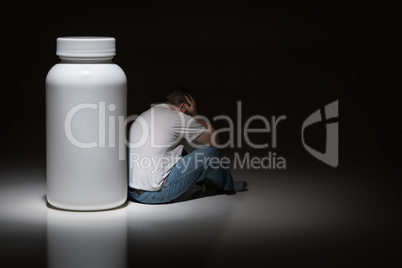 Man Holding Head Sitting Next To Blank Medication Bottle