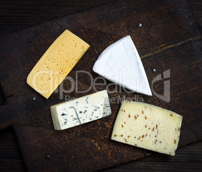 pieces of different cheeses on a brown wooden board: