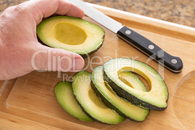 Male Hand Prepares Fresh Cut Avocado on Wooden Cutting Board