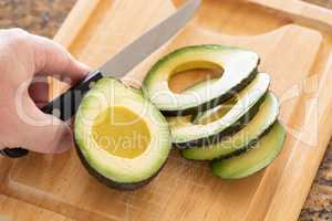 Male Hand Prepares Fresh Cut Avocado on Wooden Cutting Board