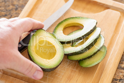 Male Hand Prepares Fresh Cut Avocado on Wooden Cutting Board