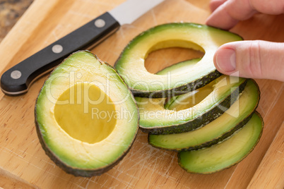 Male Hand Prepares Fresh Cut Avocado on Wooden Cutting Board