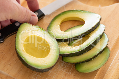 Male Hand Prepares Fresh Cut Avocado on Wooden Cutting Board