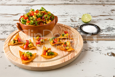 Nachos chips and vegetables in an earthenware bowl and tequila