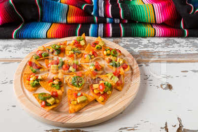 Nachos chips with vegetables on a chopping board and a poncho