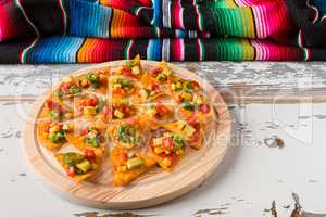 Nachos chips with vegetables on a chopping board and a poncho