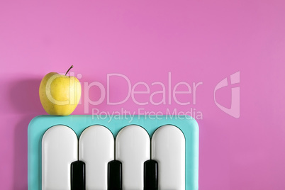 Baby blue piano music keyboard toy and yellow apple on the pink background. Minimal style concept. Punchy Pastels. Top view