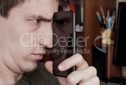 guy looks at the screen of a black smartphone, through the refle
