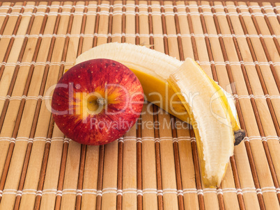 Peeled banana and red apple on wooden slats.