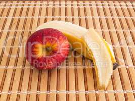 Peeled banana and red apple on wooden slats.