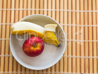 Peeled banana and apple inside white bowl.