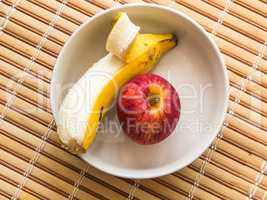 White bowl containing banana and apple, on wooden table.