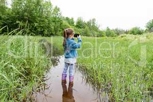 Girl stands in the water and shoots a meadow filled