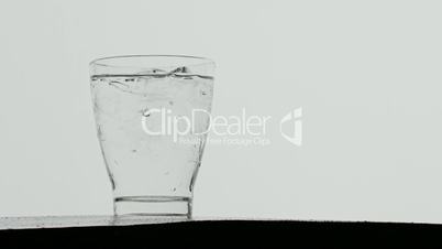 Ice cubes dropped in glass of sparkling water,